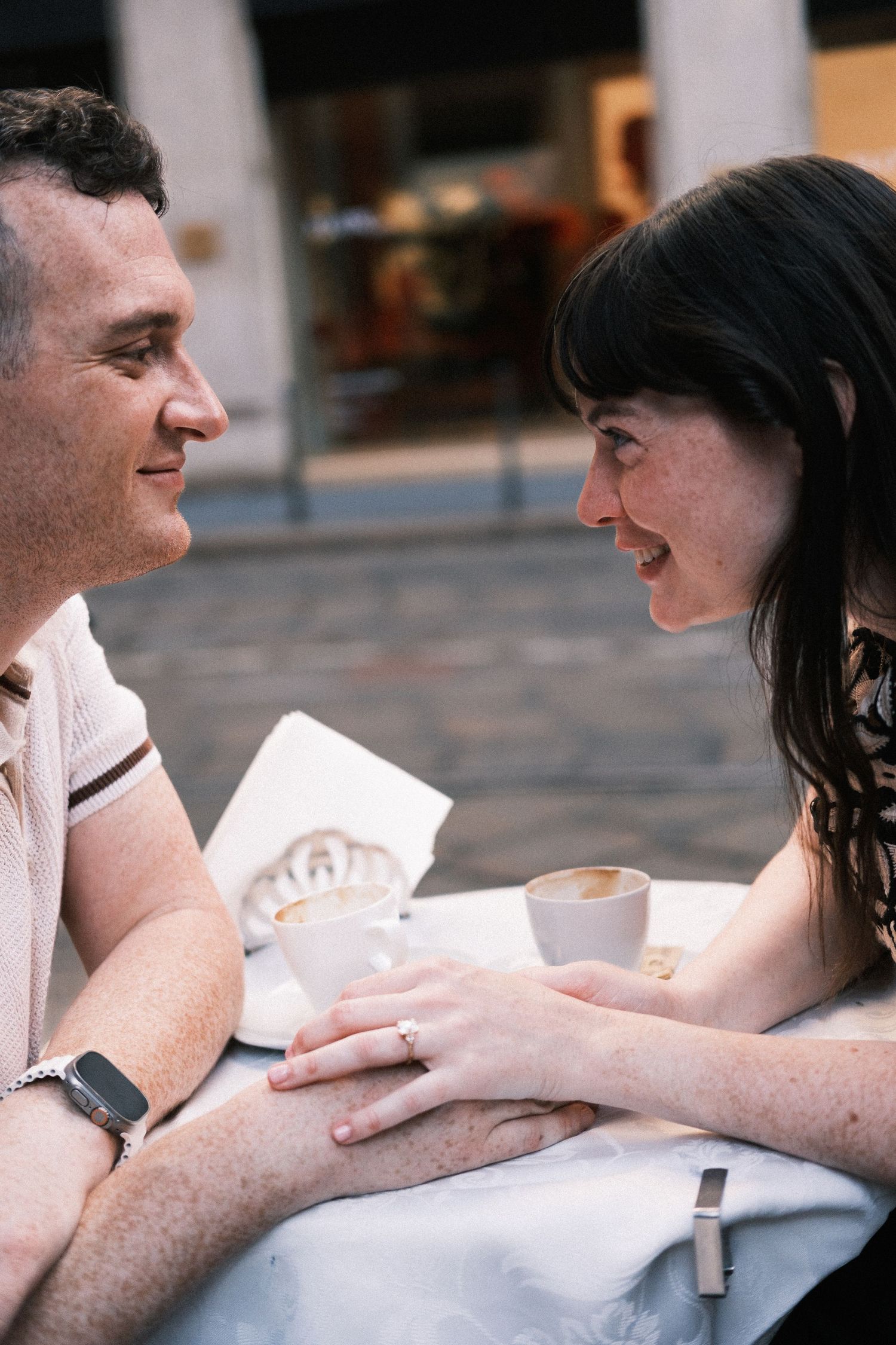 Couple holding hands and smiling at each other over coffee at an outdoor cafe table.
