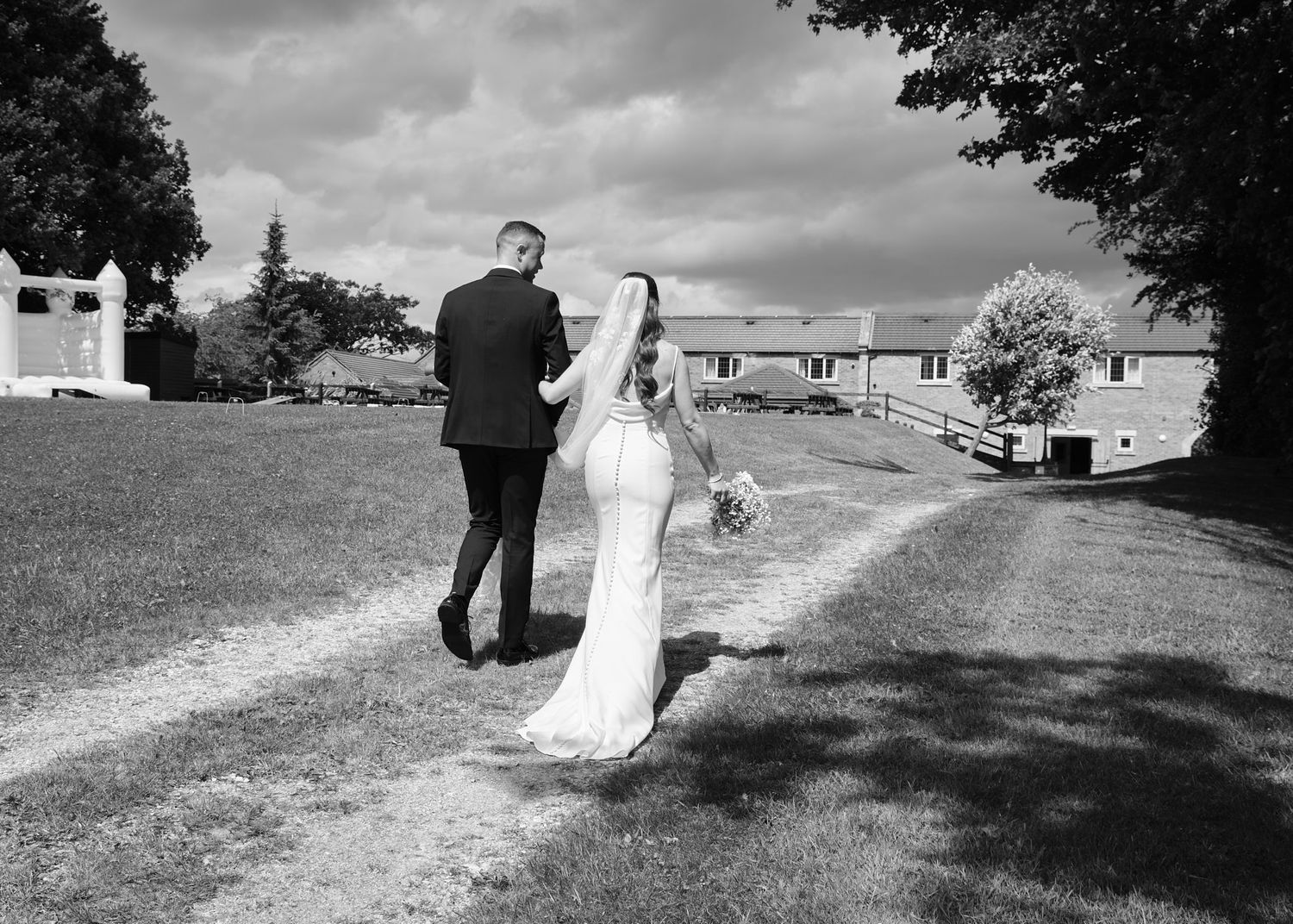 Bride and groom walking hand in hand along a path in black and white wedding photo.