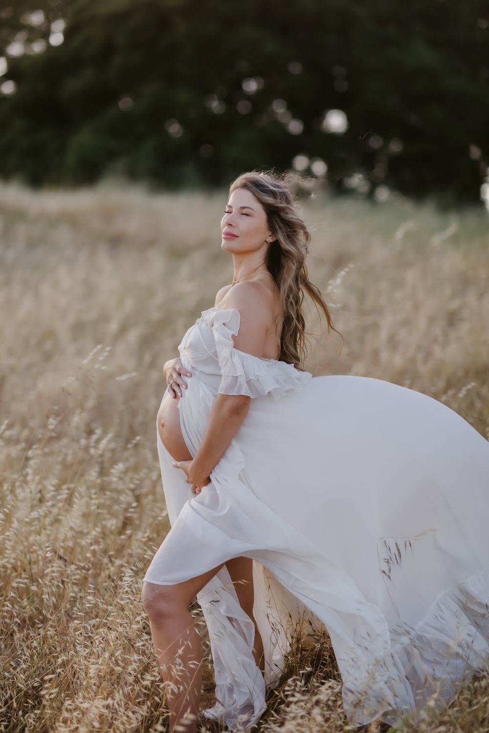 Expectant mother in white flowy gown poses with eyes closes in what field. North Conway North Shore Kennebunkport maternity photographer