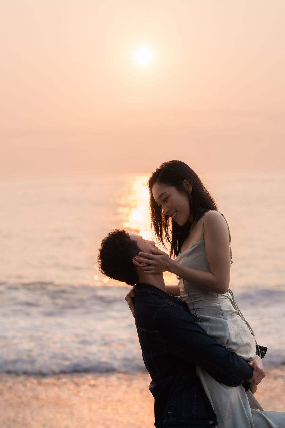 Romantic couple embracing on a beach at sunset, with golden light reflecting on the ocean waves behind them.