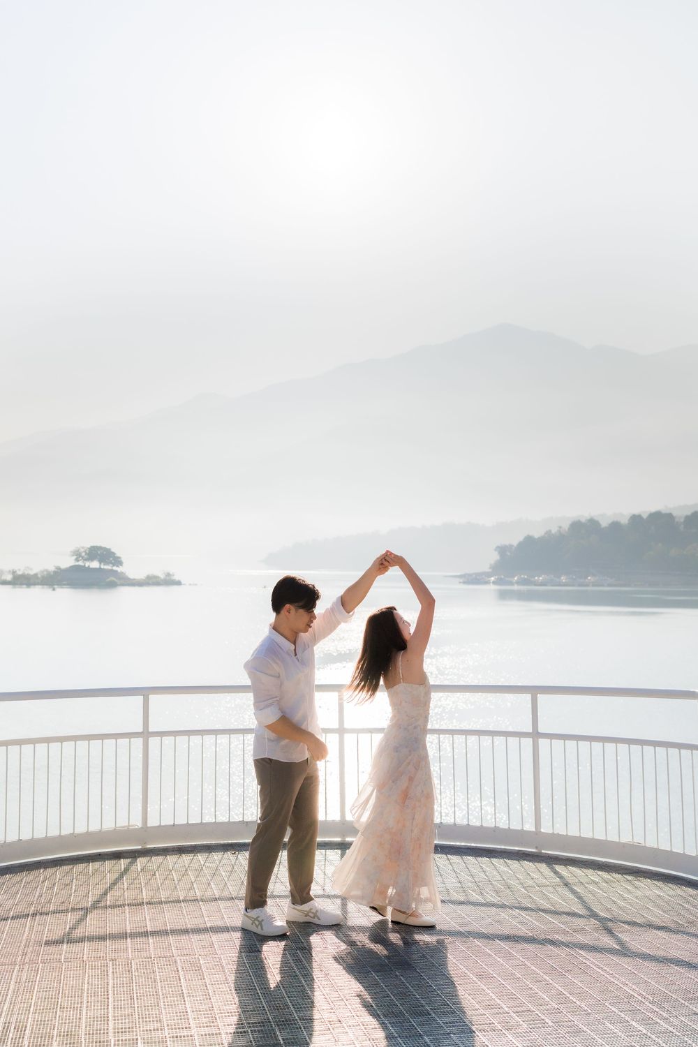 Couple dancing on scenic overlook deck with misty lake and mountain views in background.
