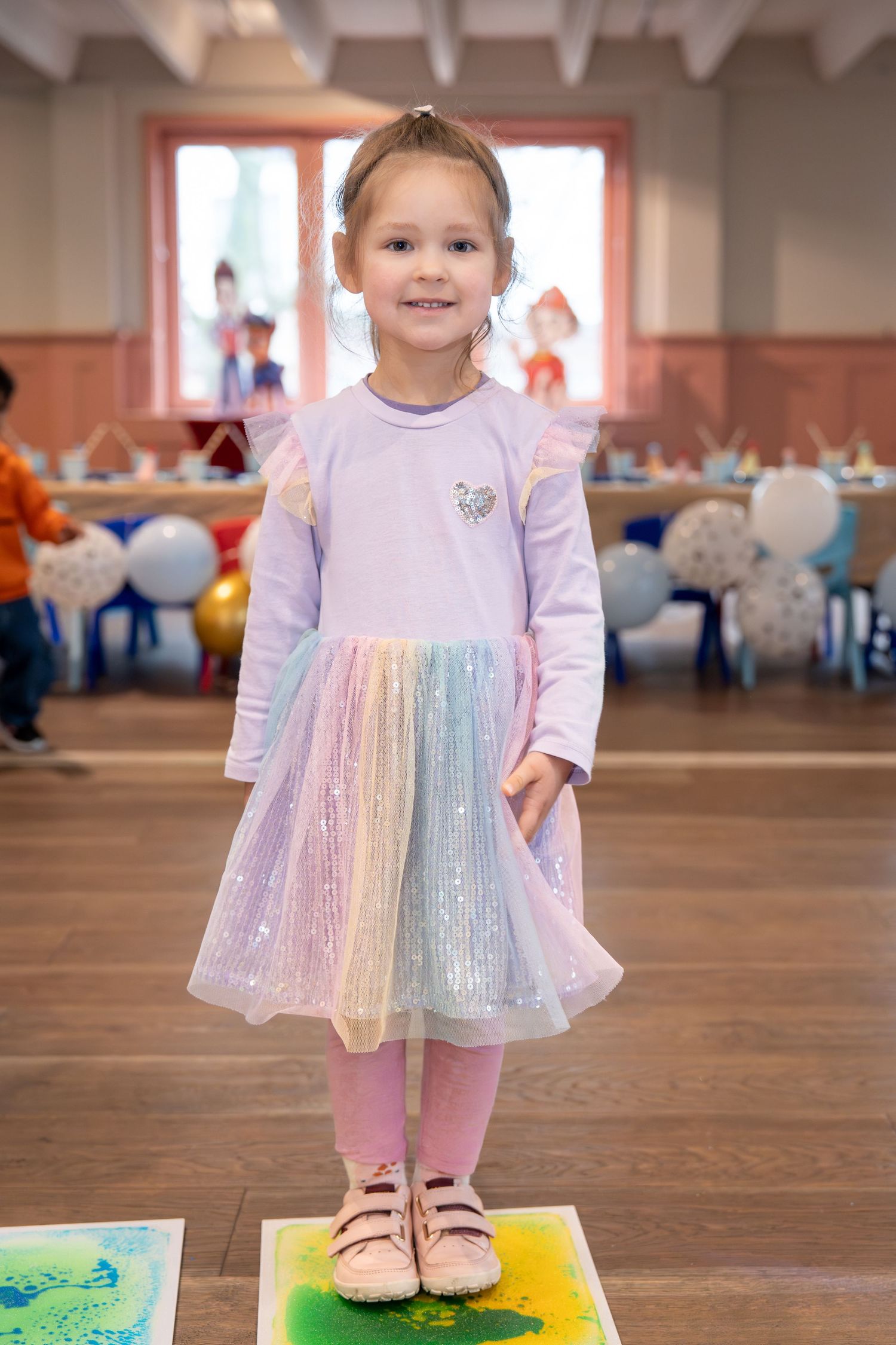 Young girl in pastel rainbow tulle dress smiling at a colorful children's party celebration.