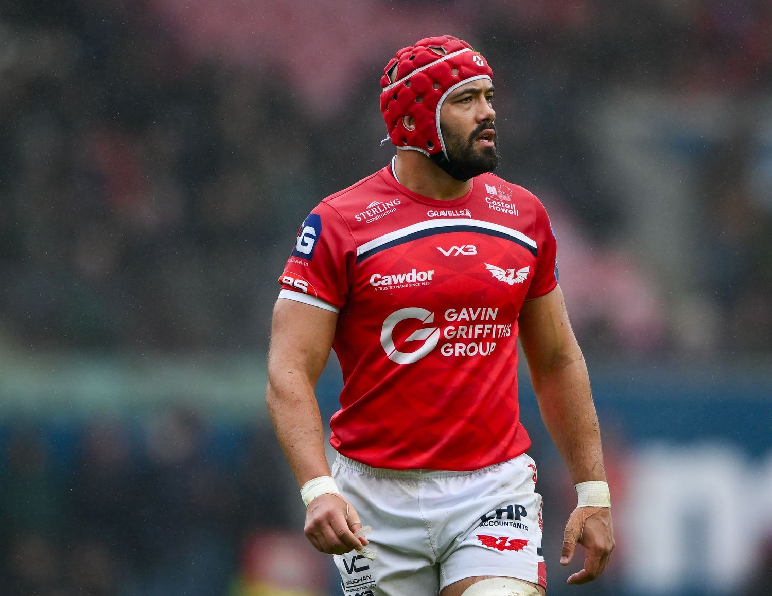 Rugby player in red Scarlets jersey with scrum cap on field during match.