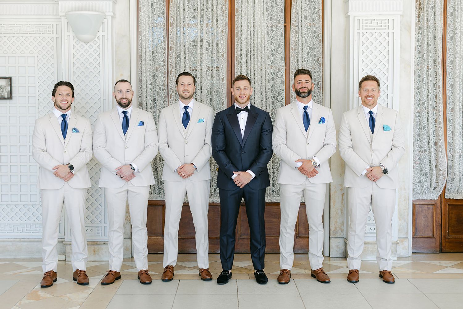 Armour House Wedding - Groom in navy suit stands with five groomsmen in light gray suits and blue ties in elegant wedding venue.