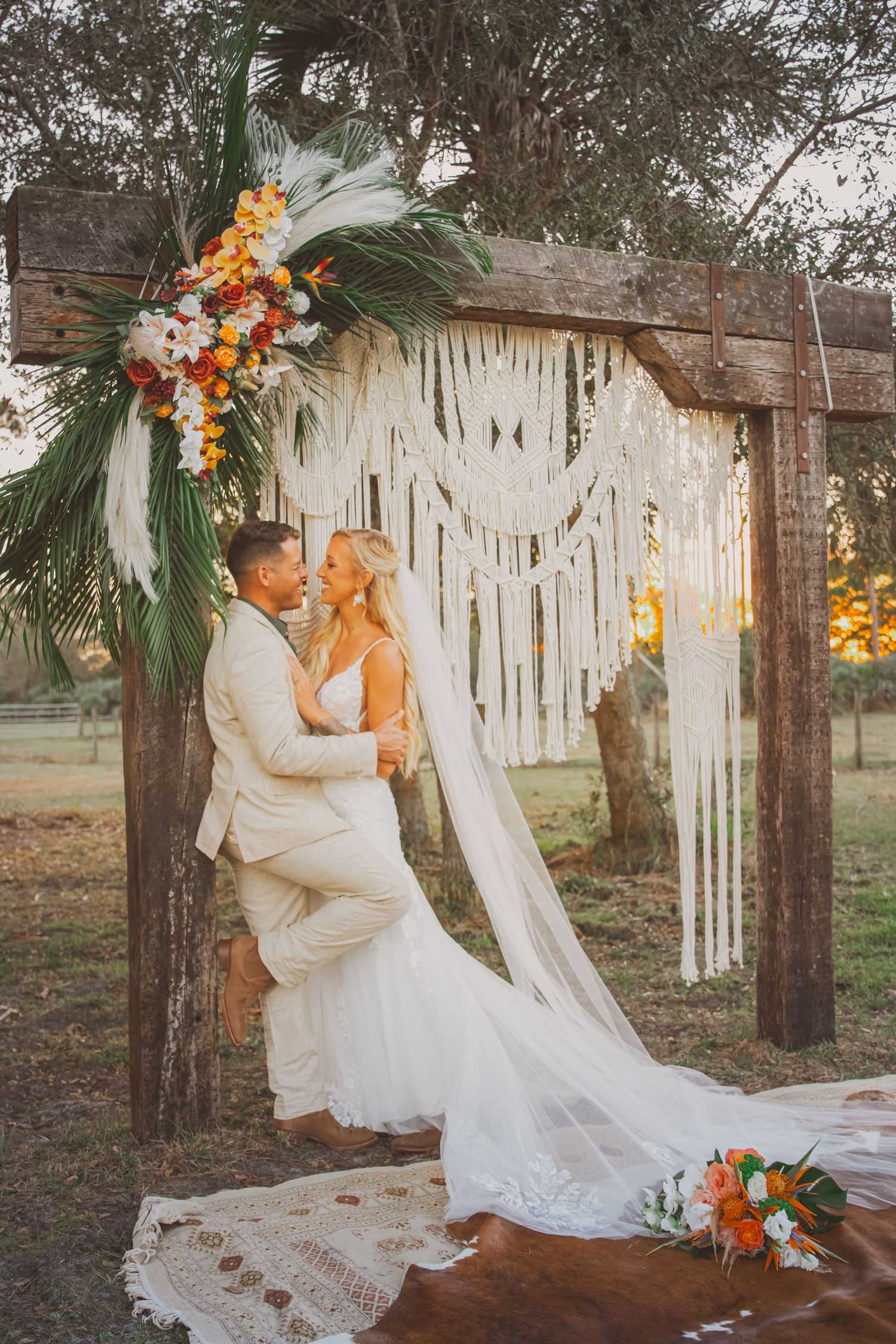 Coastal Cowgirl bridal details with a bride and groom posed against a timber arch with a macrame curtain