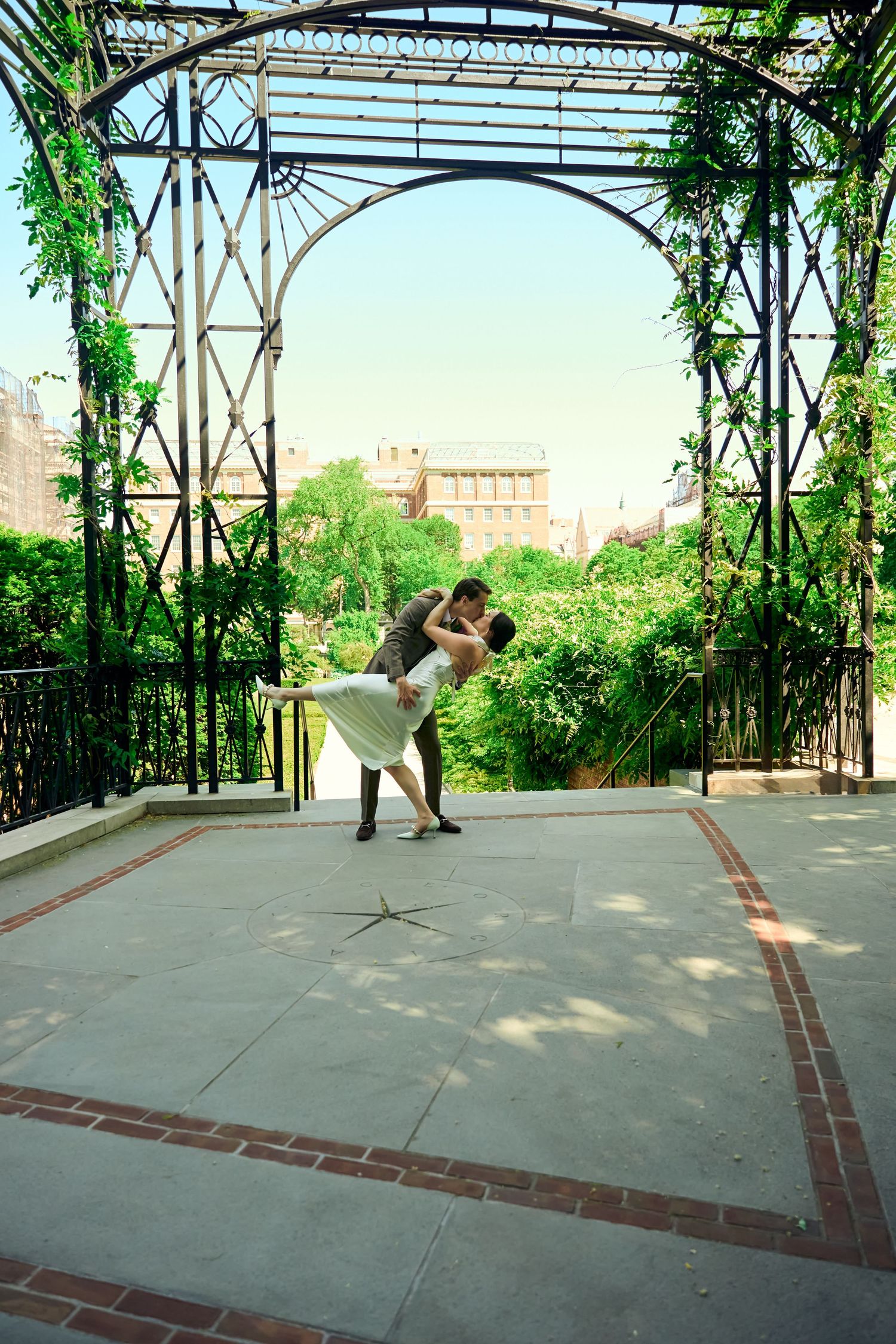 Couple sharing a romantic dip kiss under an iron pergola with lush greenery in an outdoor garden setting.