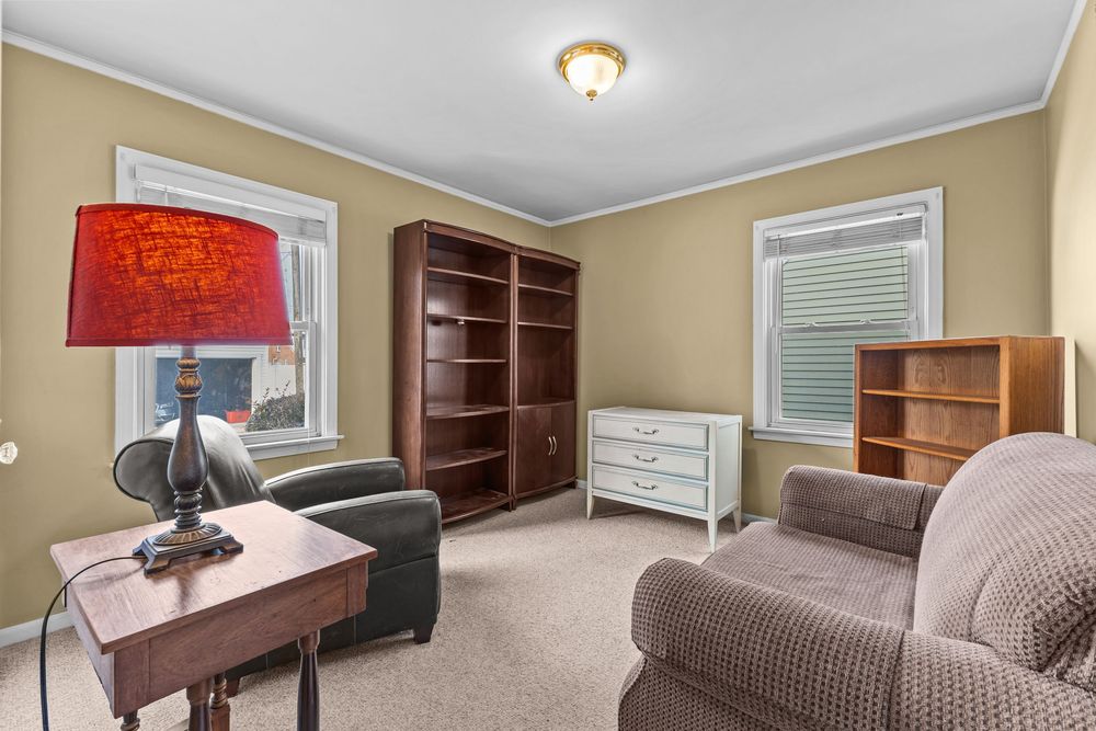 Casual living room with red lamp, built-in bookshelves, and comfortable seating on neutral carpet.