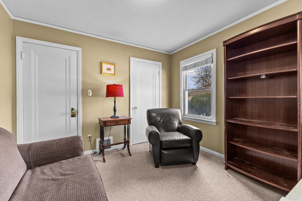 Relaxing sitting room with leather armchair, bookshelf, crown molding, and neutral carpet flooring.
