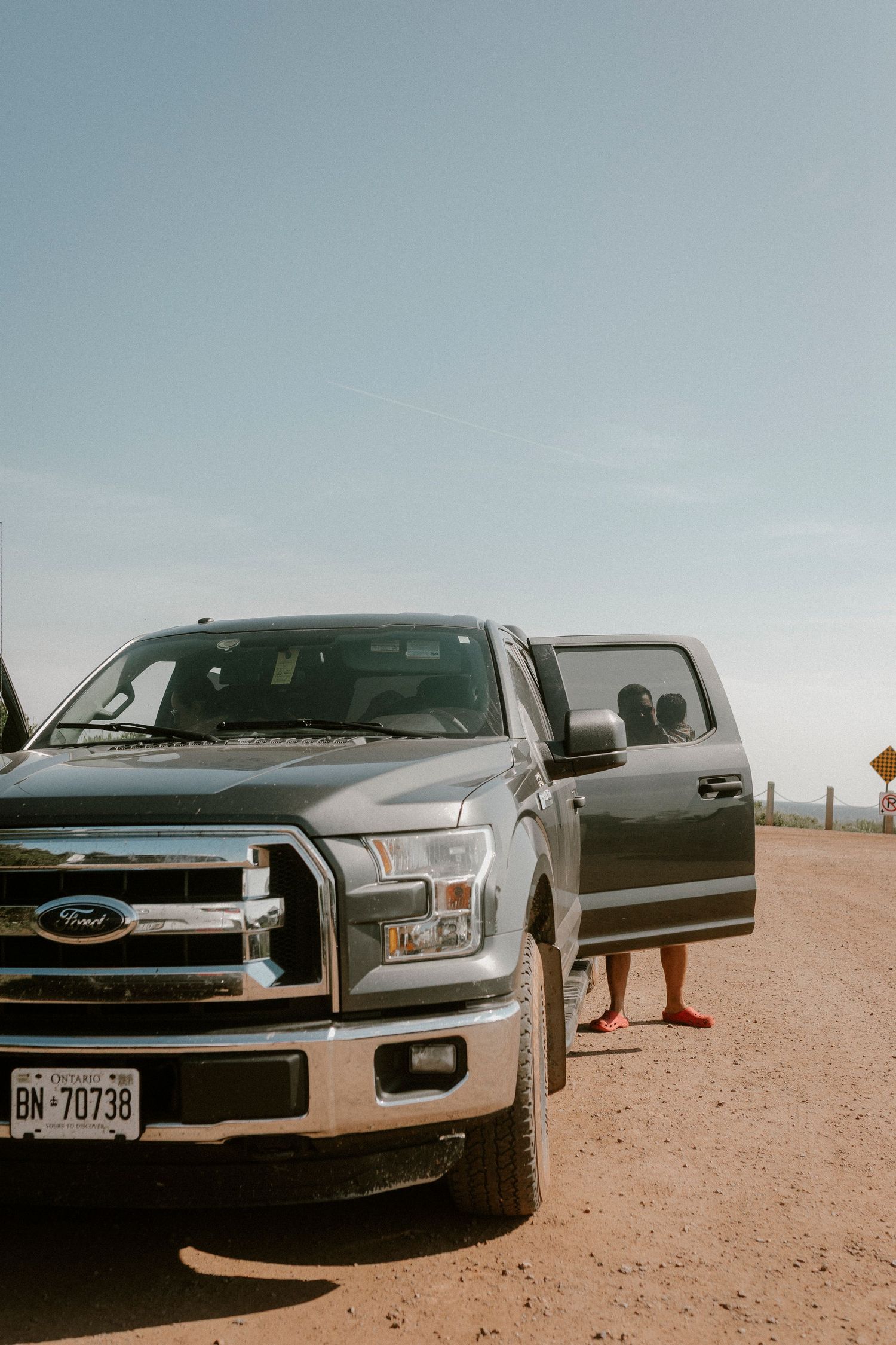 Gray Ford F-150 pickup truck with Ontario plates parked on red dirt road under clear blue sky.