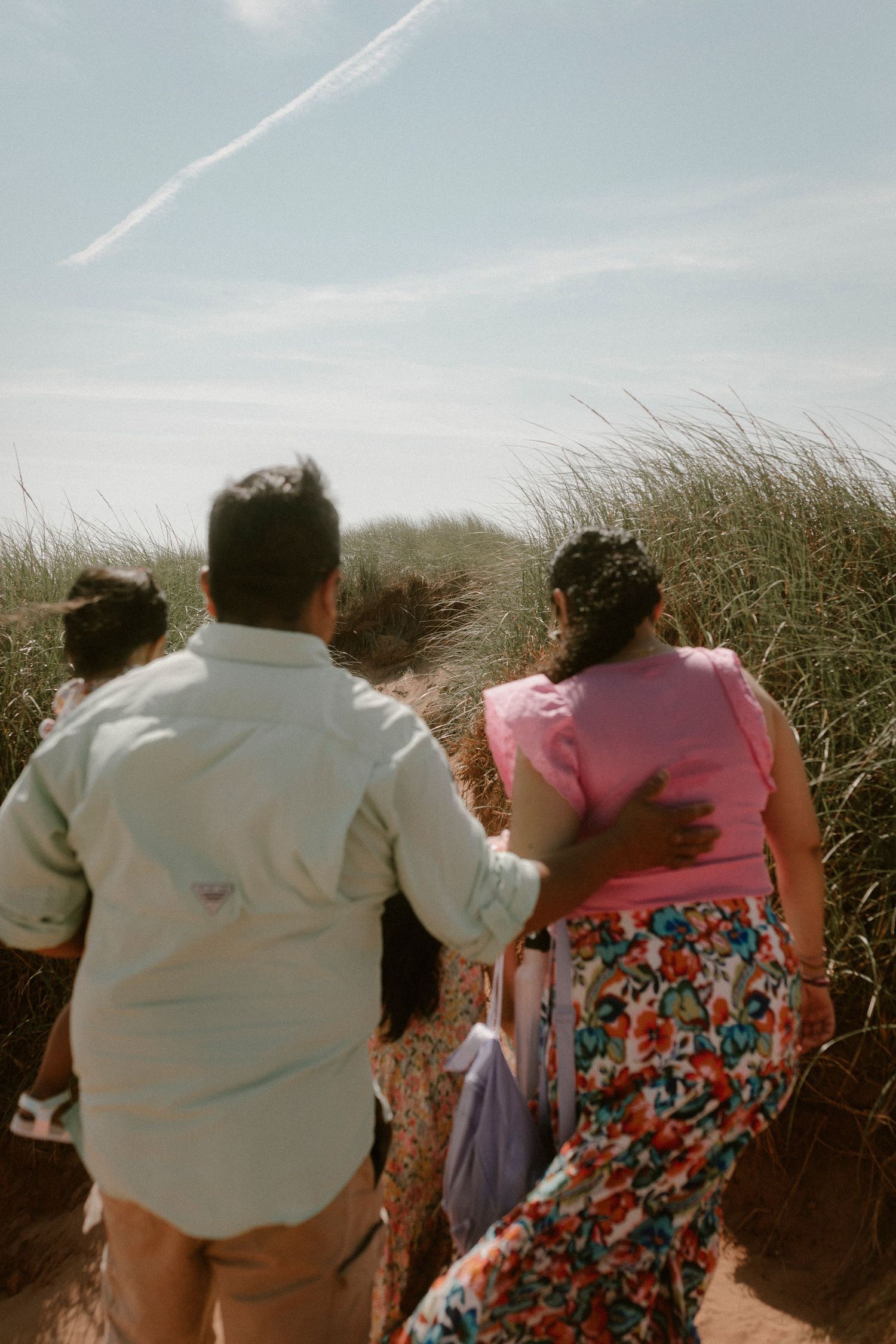 Family walking together through coastal sand dunes on a bright sunny day.