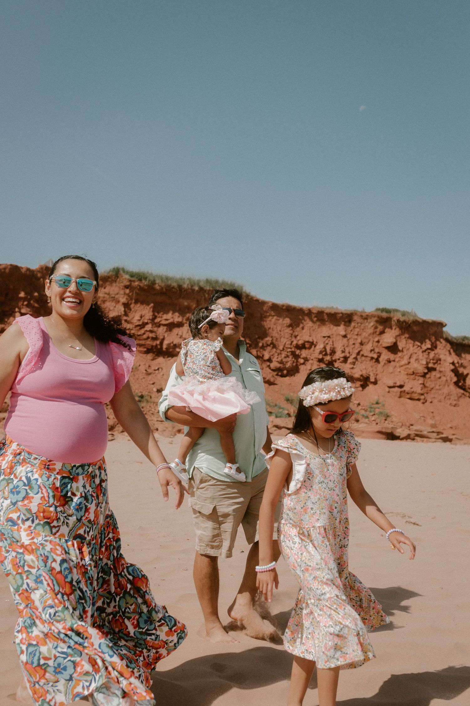 Happy family walking on PEI red sand beach with coastal cliffs in background.