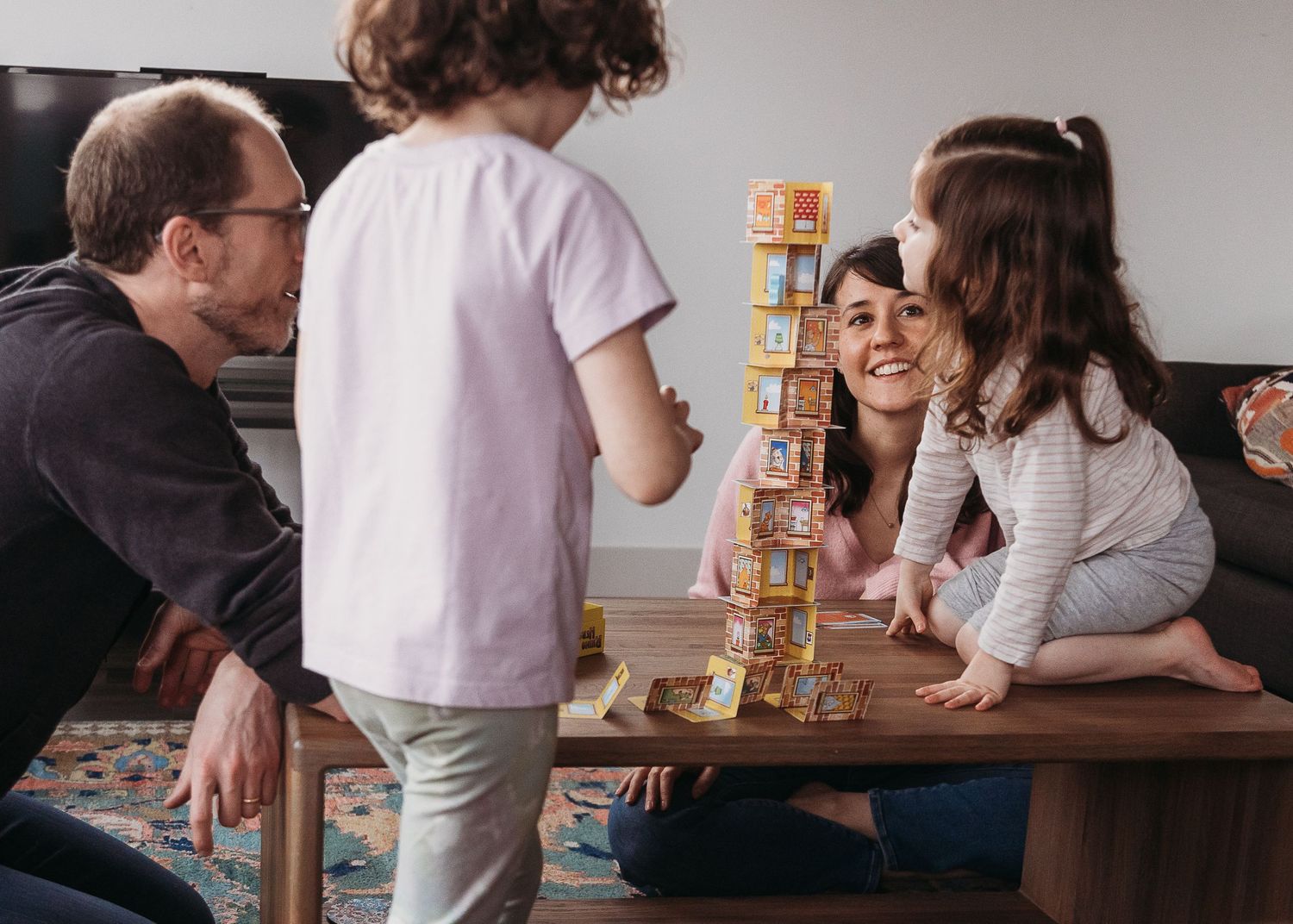 Family playing a stacking block tower game together at a coffee table, laughing and having fun indoors.