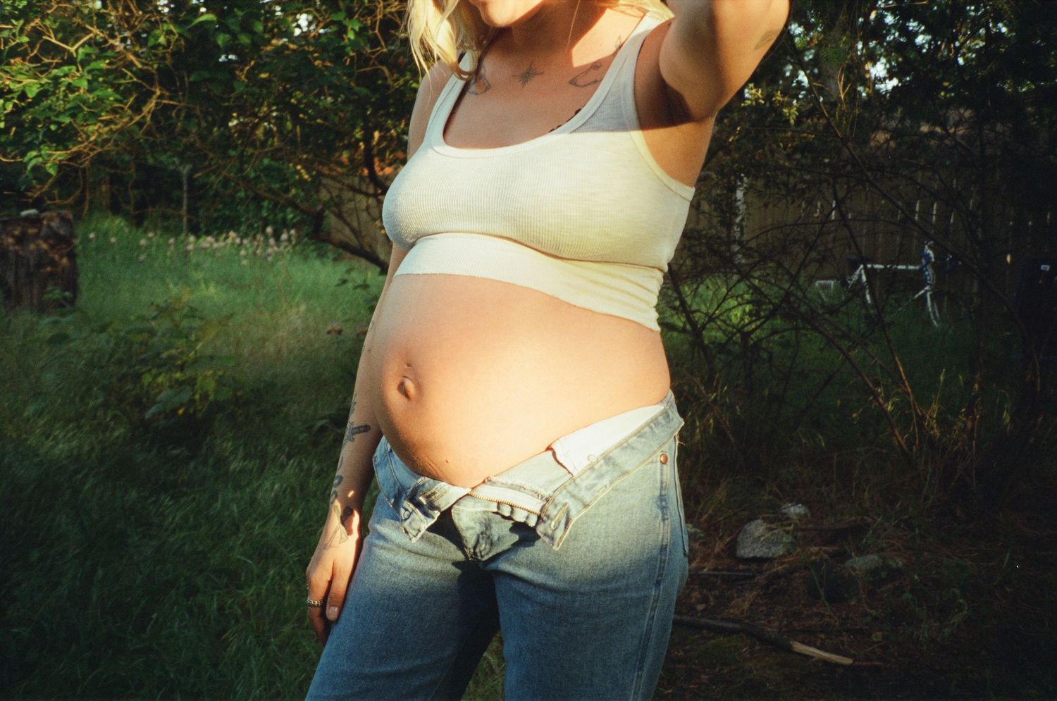Close-up of a pregnant woman in a crop top and jeans showing her baby bump outdoors.