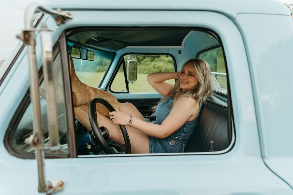 Smiling blonde woman relaxing in classic baby blue truck cab during outdoor photo session.