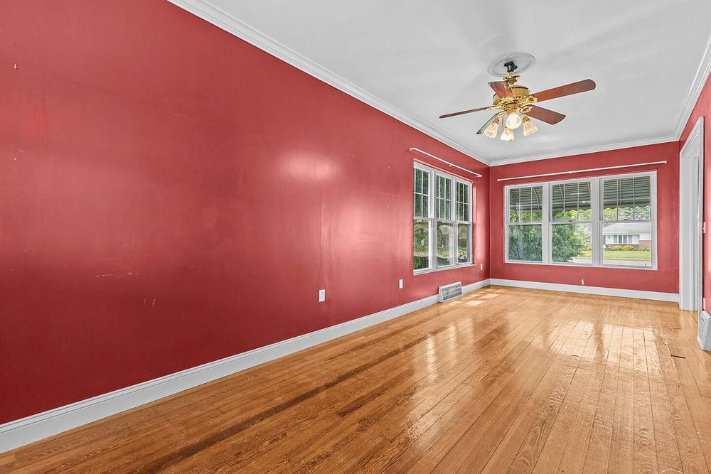 Spacious room with bold red walls, hardwood floors, ceiling fan, and white trim windows.