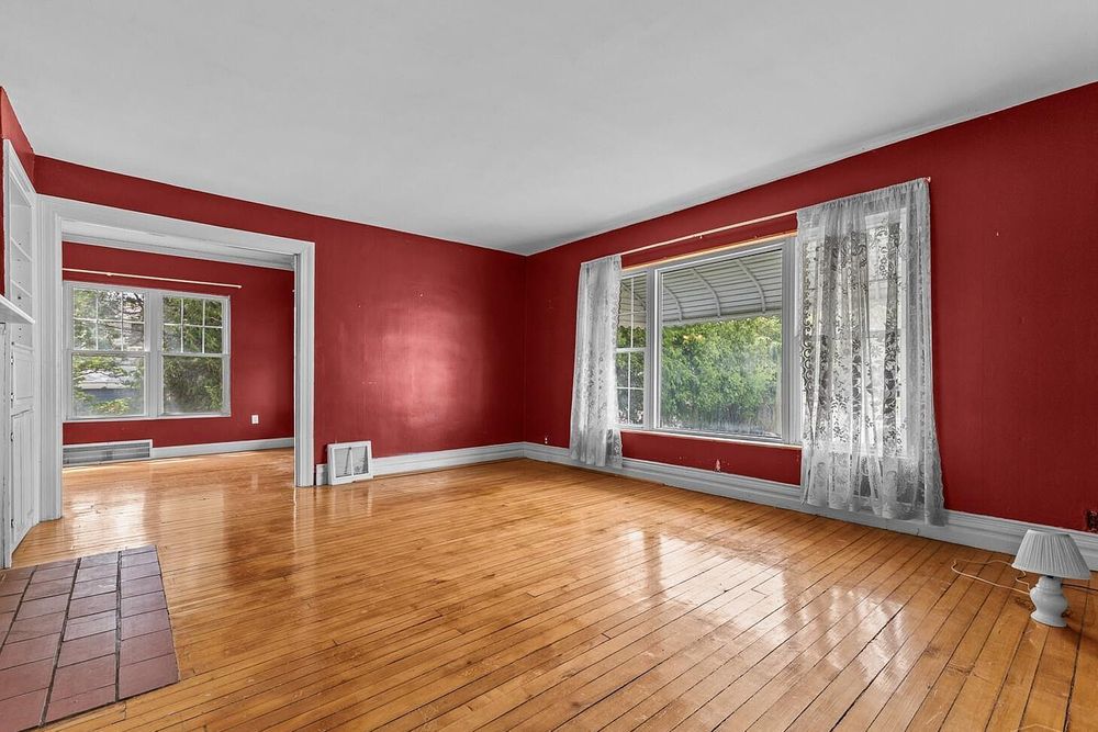 Open living space featuring rich red walls, gleaming hardwood floors, and multiple bright windows.