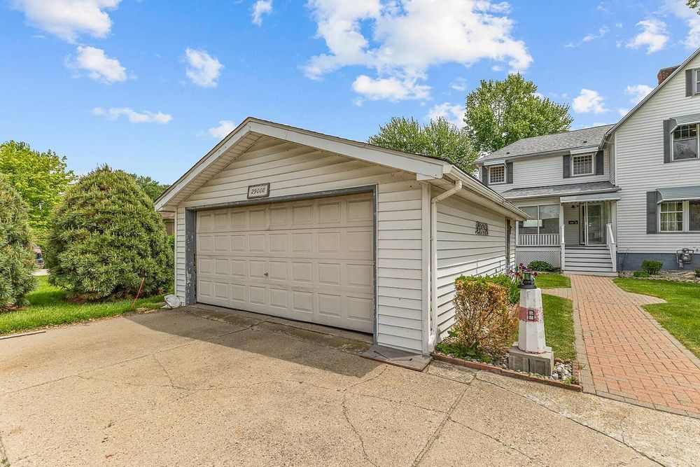 Detached two-car garage with white siding and brick driveway beside a two-story suburban home.