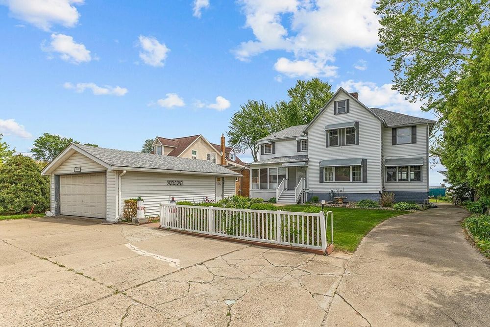 Large two-story white colonial home with detached two-car garage, white picket fence, and mature trees on a spacious lot.