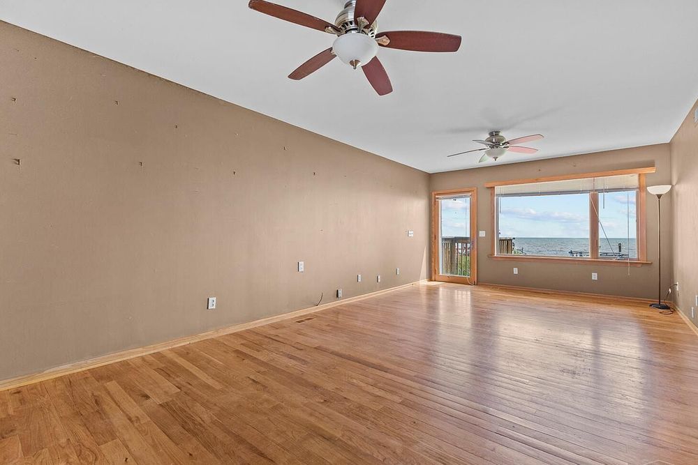 Bright empty living room with hardwood floors, ceiling fan, and large windows offering scenic views.