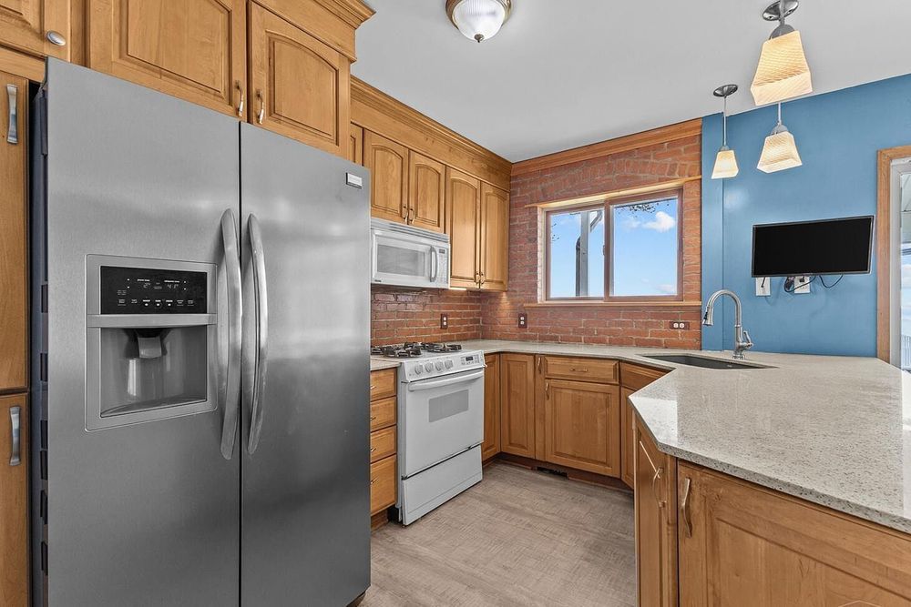 Modern kitchen with stainless steel refrigerator, white gas range, oak cabinets, and tile backsplash.