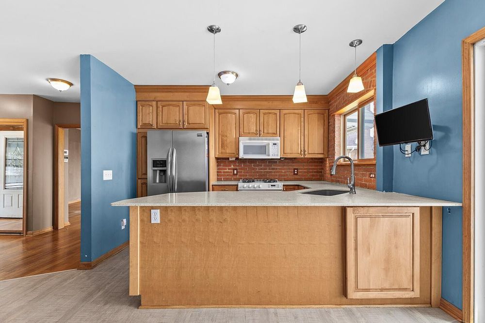 Open kitchen with oak island, stainless appliances, pendant lights, and blue accent walls.