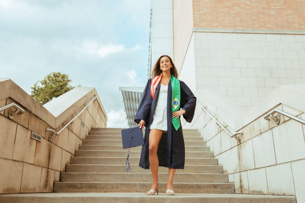 Female graduate in black cap and gown walking down outdoor university steps.