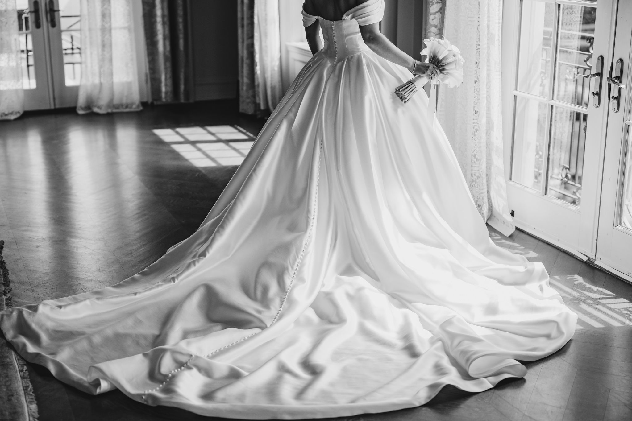 Black and white photo of bride in stunning off-shoulder wedding gown with long cathedral train.