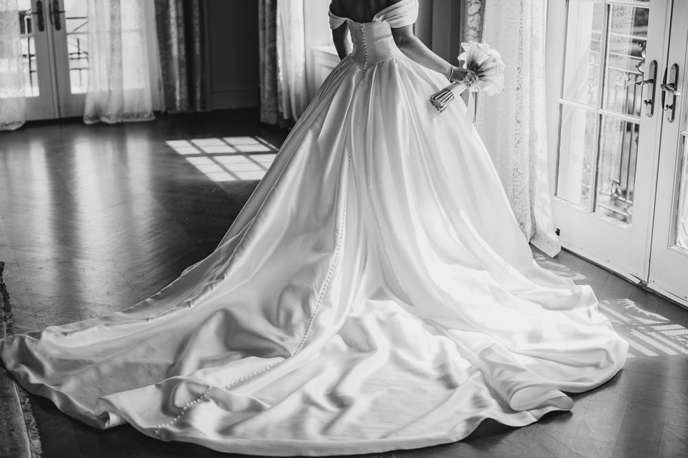 Black and white photo of bride in stunning off-shoulder wedding gown with long cathedral train.