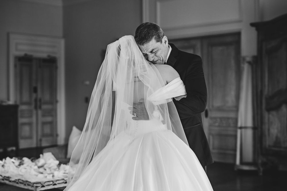 Black and white photo of groom tenderly embracing bride in wedding gown and veil indoors.