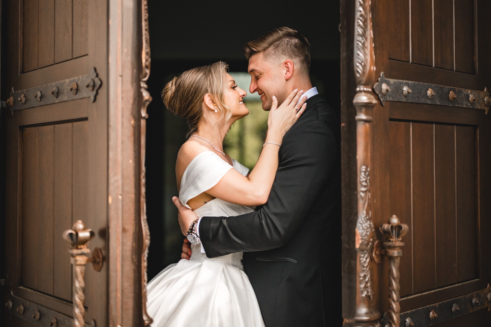 Bride and groom share an intimate moment framed by ornate carved wooden doors.