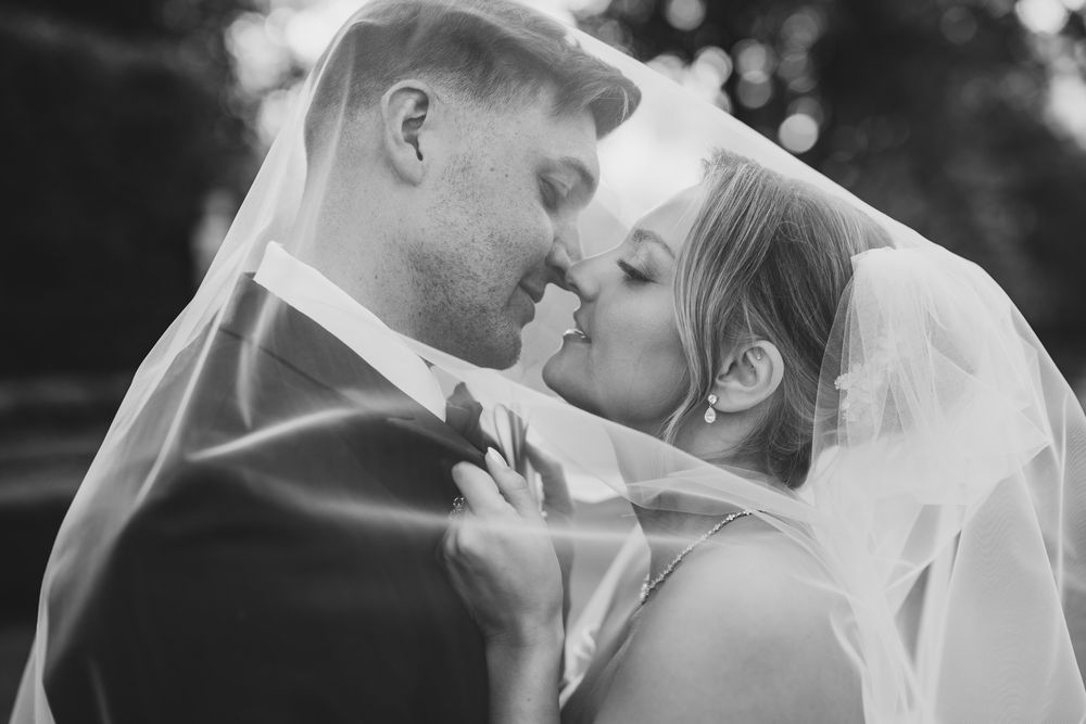 Romantic black and white photo of bride and groom almost kissing under a flowing veil.