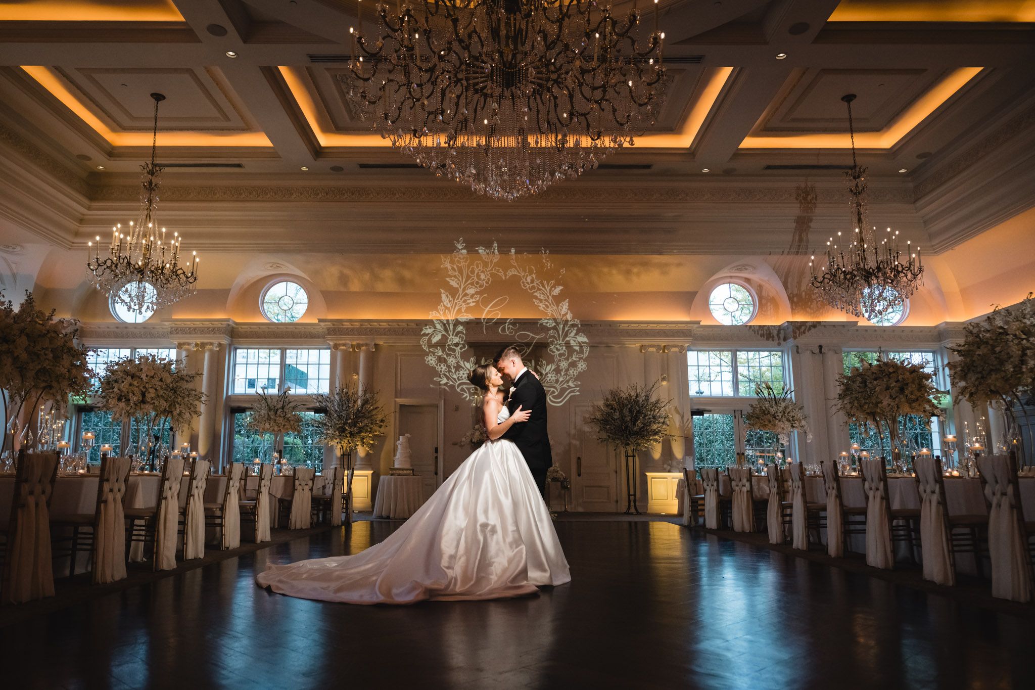 Bride and groom share romantic kiss under grand chandeliers in elegant ballroom.