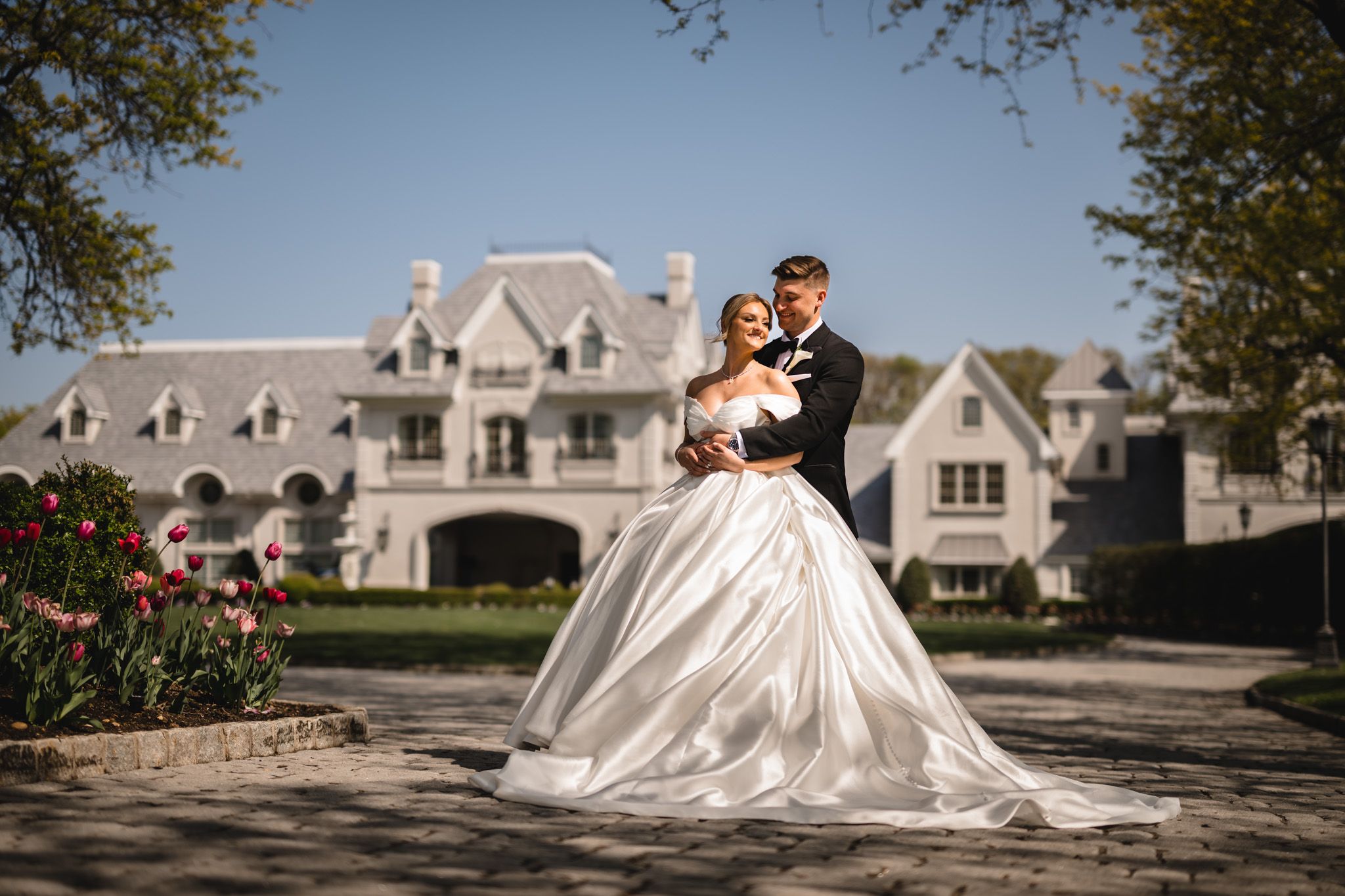 Elegant bride and groom pose in front of a grand estate mansion on their wedding day.