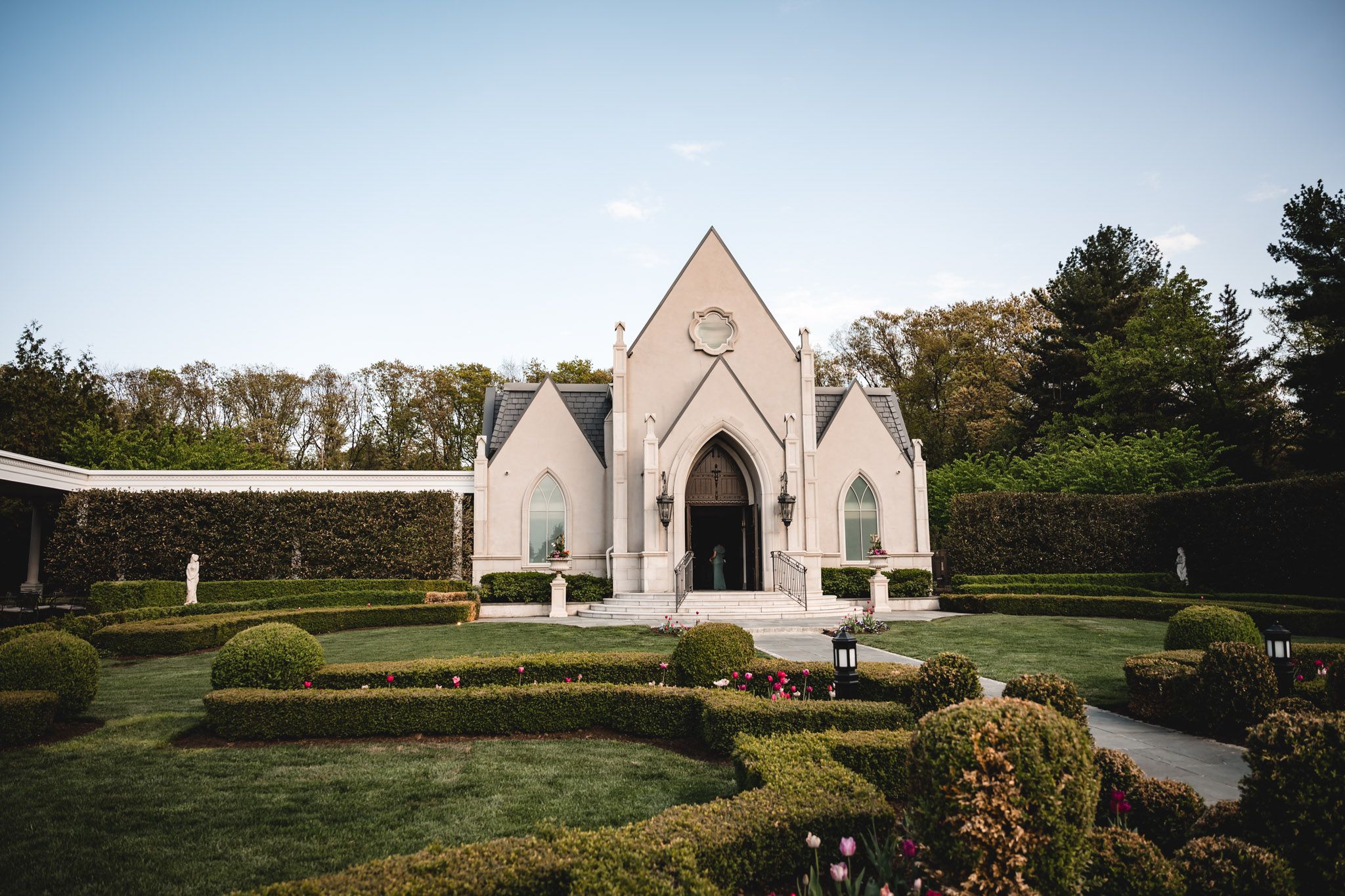 Elegant white Gothic-style wedding chapel surrounded by manicured hedges and lush greenery.