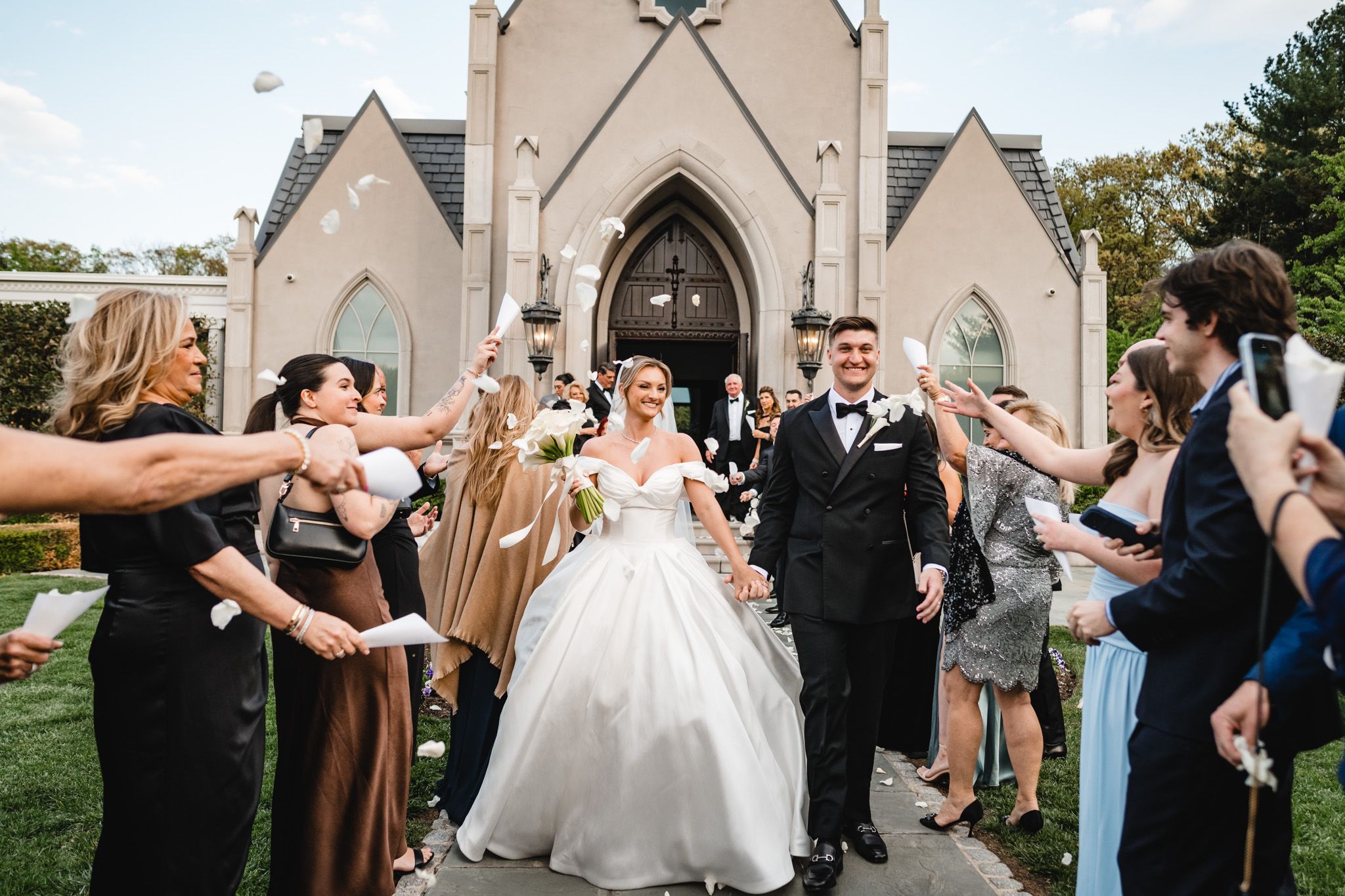 Bride and groom exit Gothic chapel as guests celebrate with confetti and streamers.