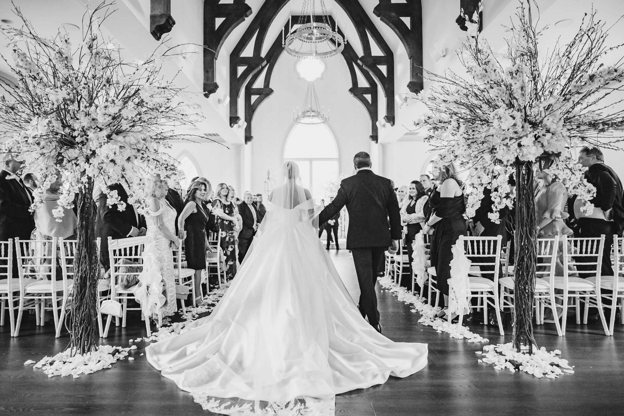 Bride walks down aisle in stunning cathedral with floral arrangements in black and white.