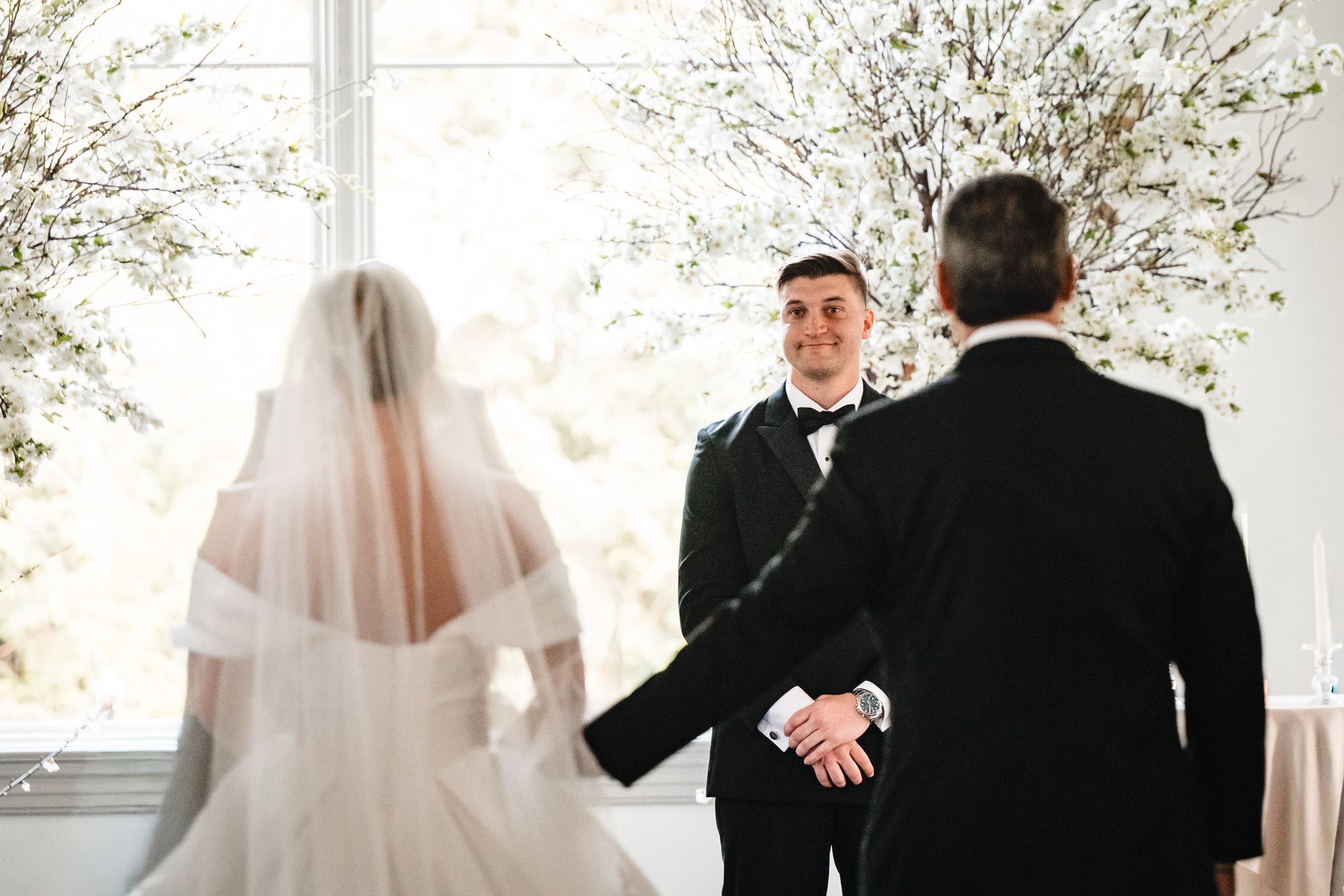 Groom smiling at bride in white gown and veil during intimate wedding ceremony at the altar.