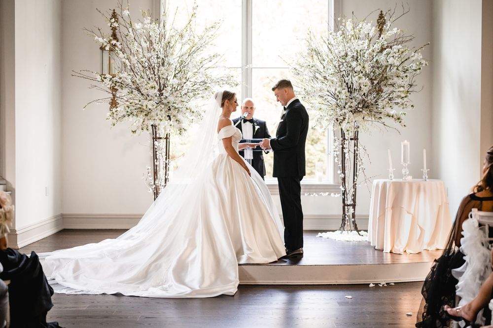 Bride and groom exchange vows at elegant indoor wedding ceremony with white floral arrangements.