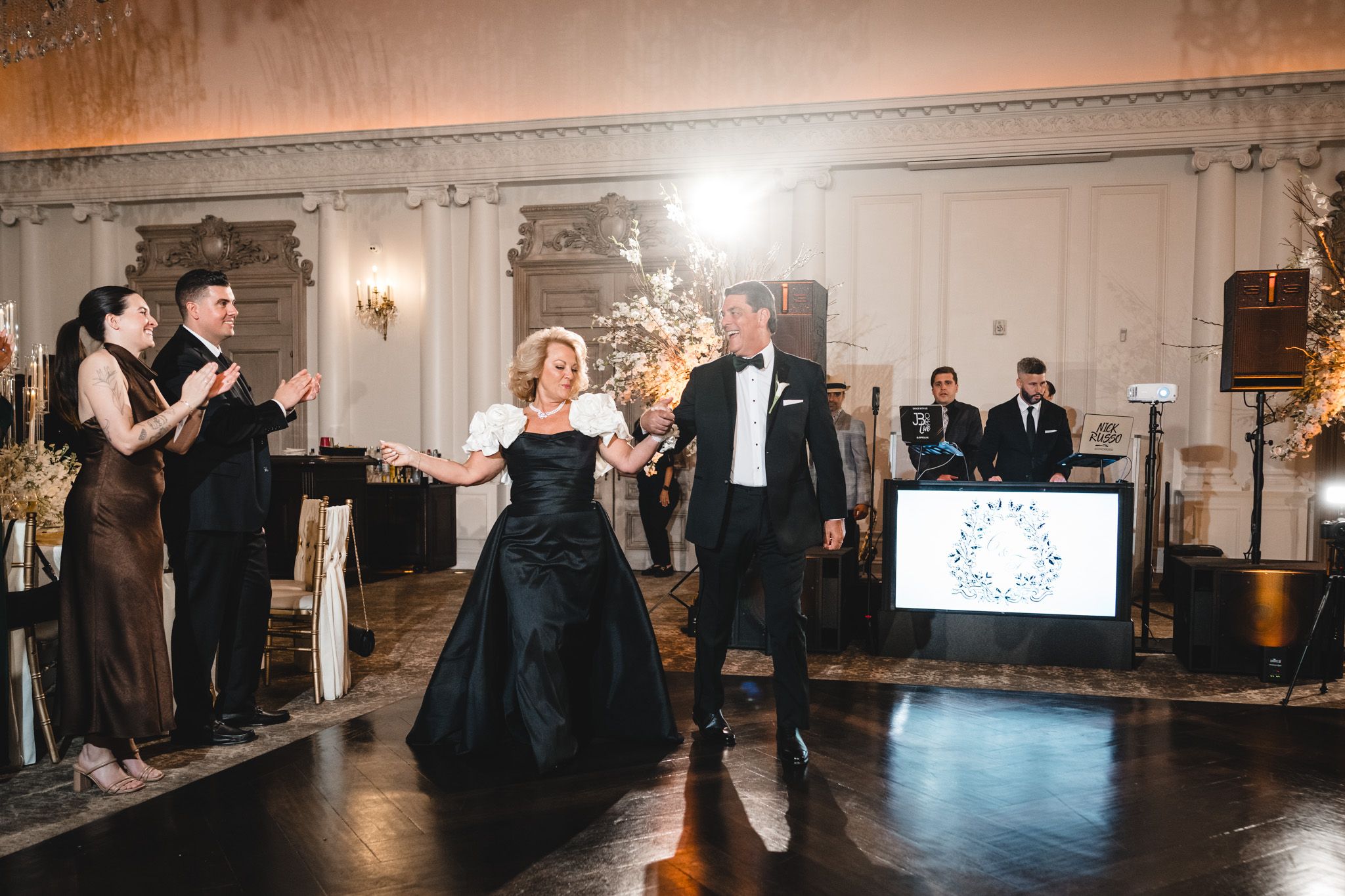 A woman in a black gown and man in tuxedo share a dance at an elegant wedding reception.