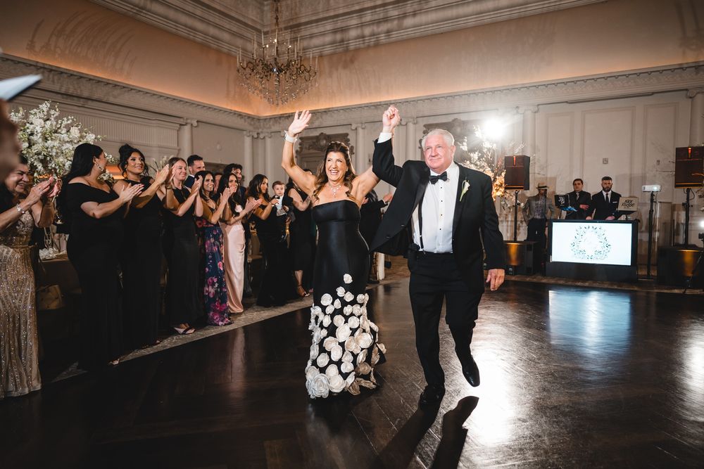 Couple in black formal wear making grand entrance into elegant wedding reception ballroom.