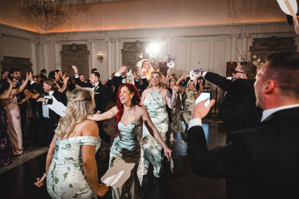 Bridesmaids in floral dresses dancing energetically with wedding guests on the reception floor.