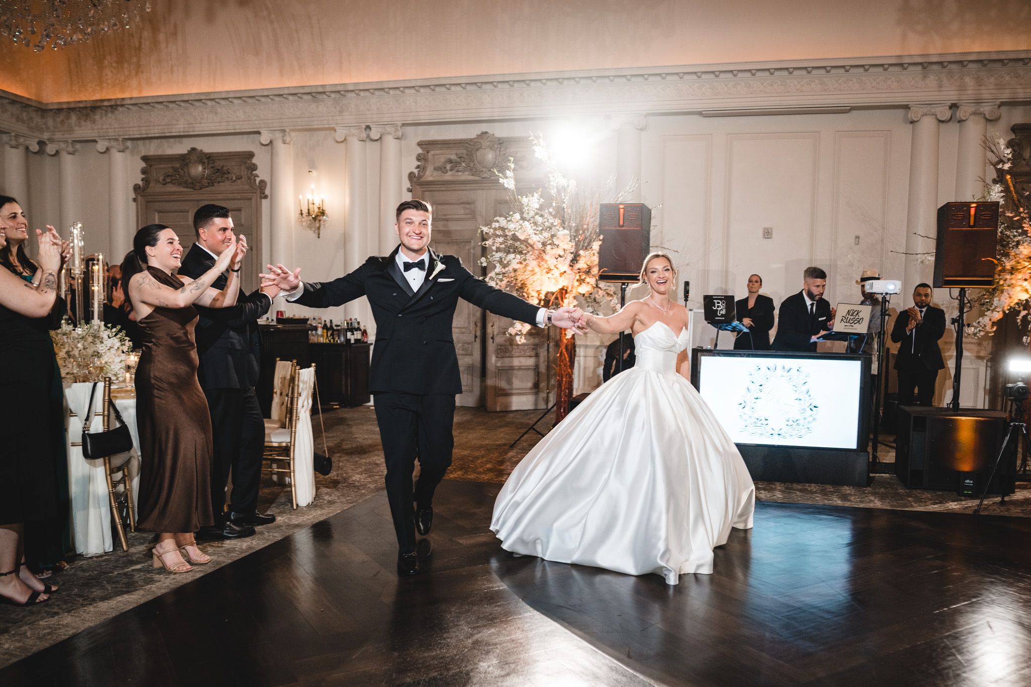 Newlyweds make a grand entrance onto the dance floor surrounded by cheering guests and sparkling lights.