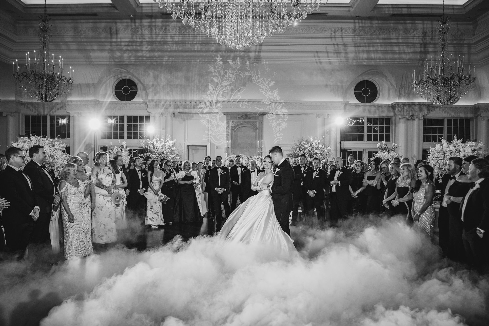 Bride and groom share first dance surrounded by dry ice fog and chandelier lighting.