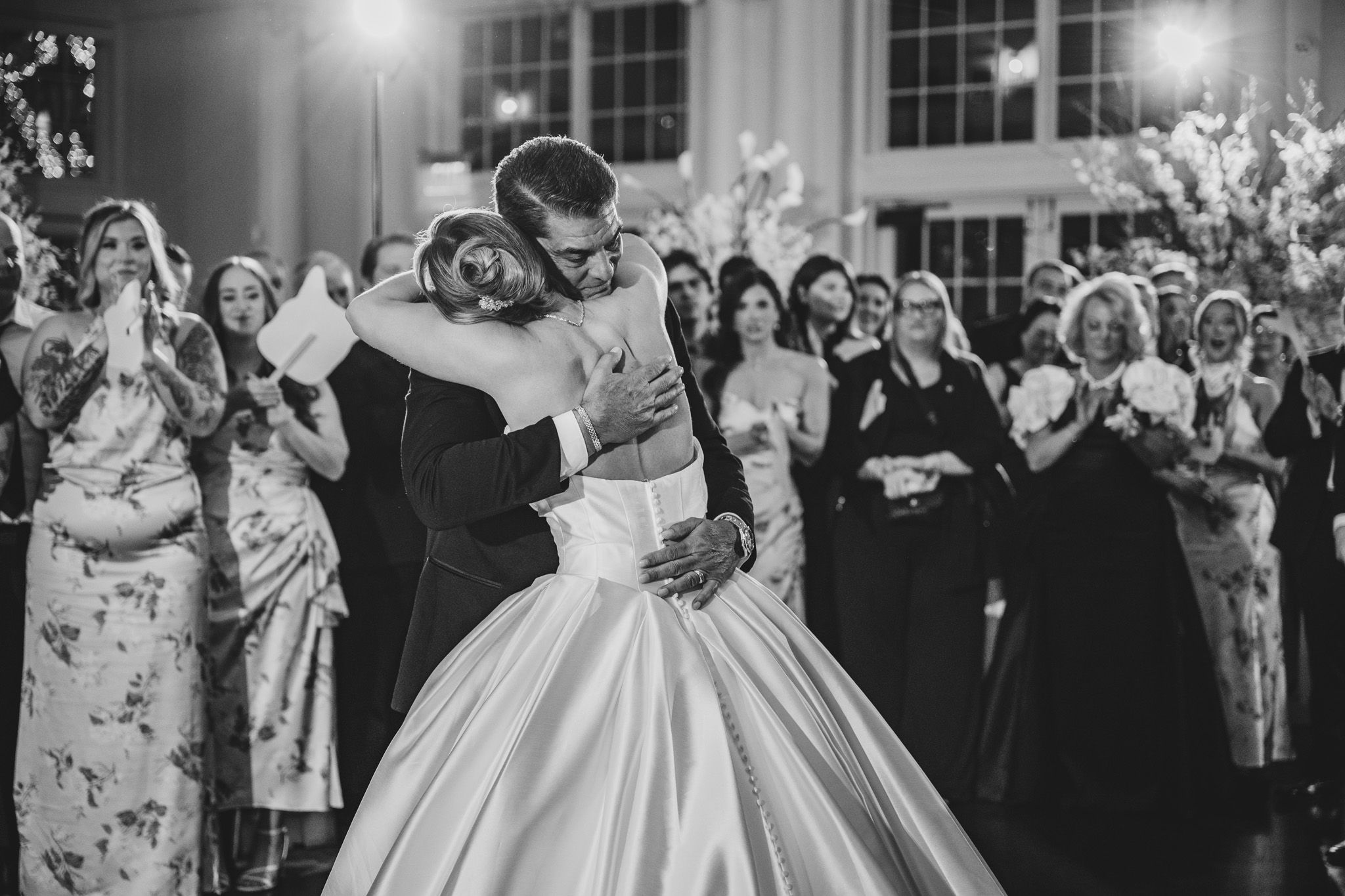 Bride and groom share emotional first dance embrace in black and white wedding reception photo.