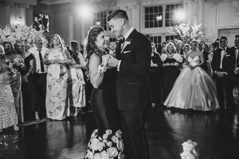 Bride and groom share first dance at elegant wedding reception while guests watch in black and white photo.
