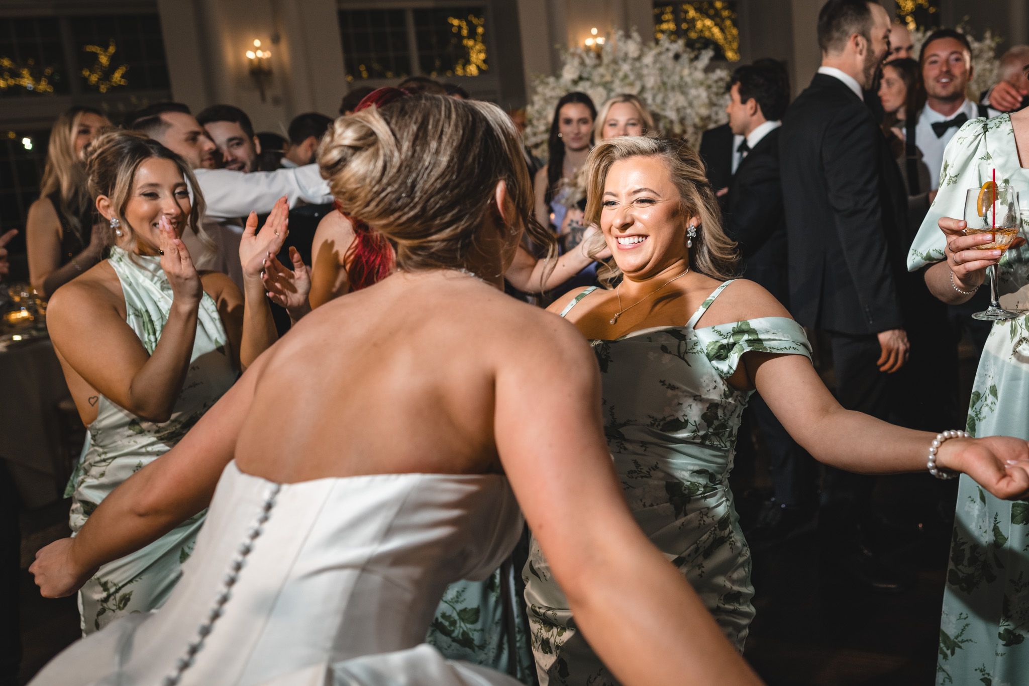 Bridesmaids in sage green gowns dance and celebrate with bride at wedding reception.