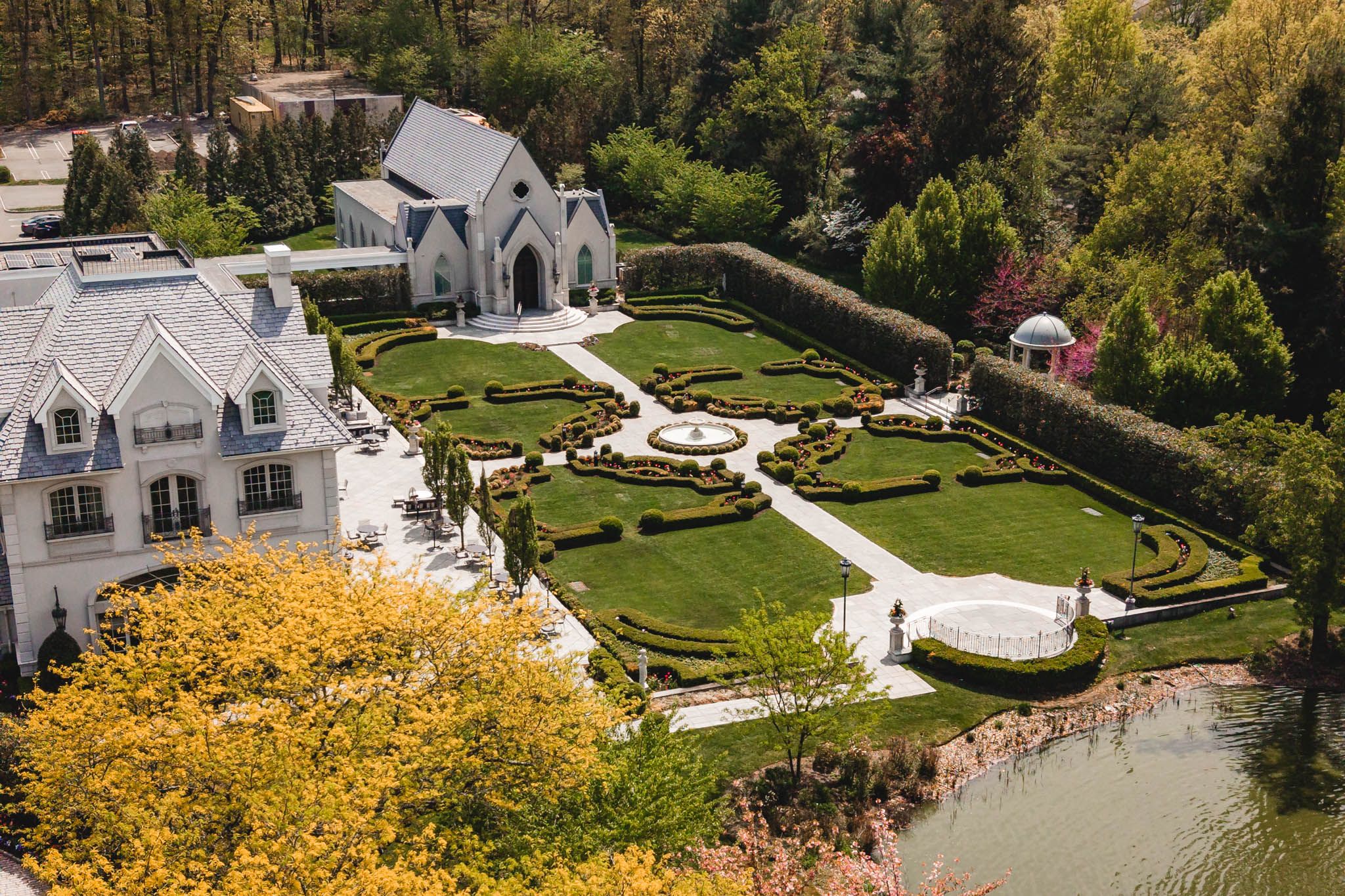 Aerial view of grand estate with manicured French formal gardens, fountain, and chapel venue.