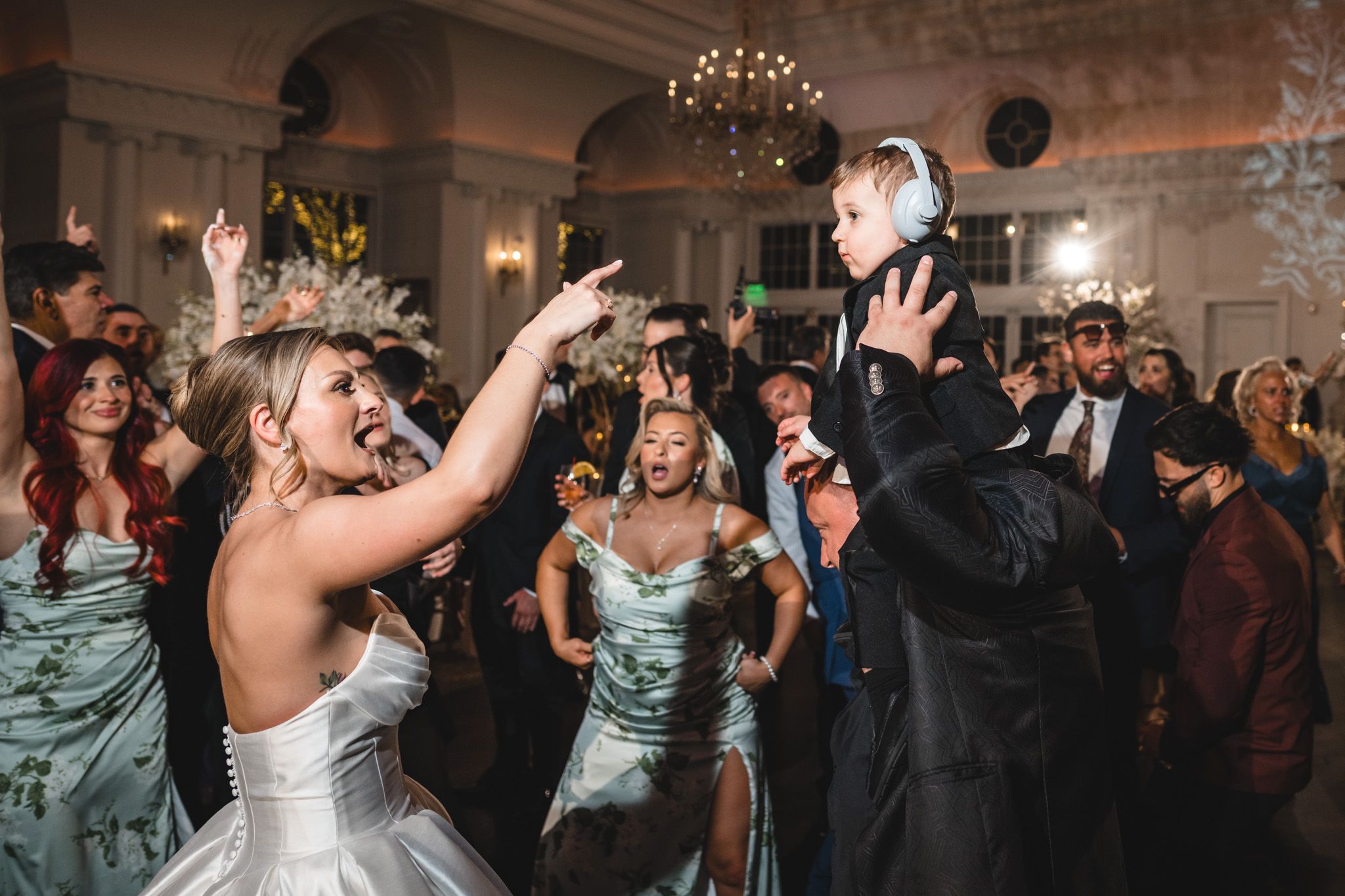 Bride dances joyfully with child wearing headphones at lively wedding reception celebration.