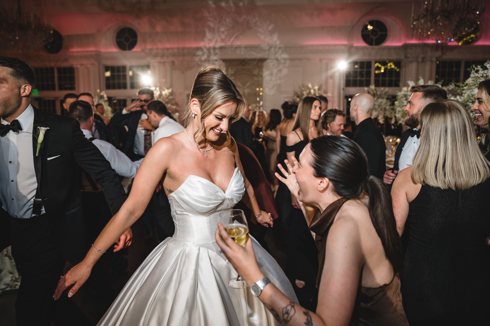 Bride in strapless satin gown dancing joyfully with guest at wedding reception.