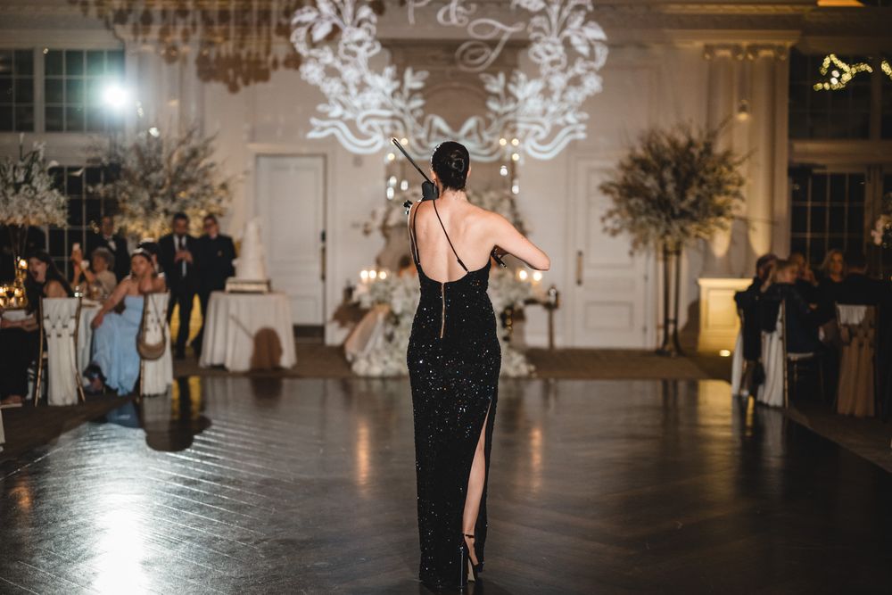Elegant woman in black backless gown performs at luxury wedding reception in ornate ballroom.